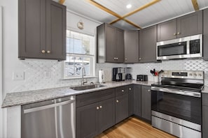 A modern kitchen with grey cabinets, stainless steel appliances, a dishwasher, and a window with blinds.