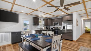 A modern kitchen with dark cabinets, stainless steel appliances, and a dining area with a wooden table and chairs. - Nautical Miles Home, Close to Park, Beach & Shops (Cape Charles)