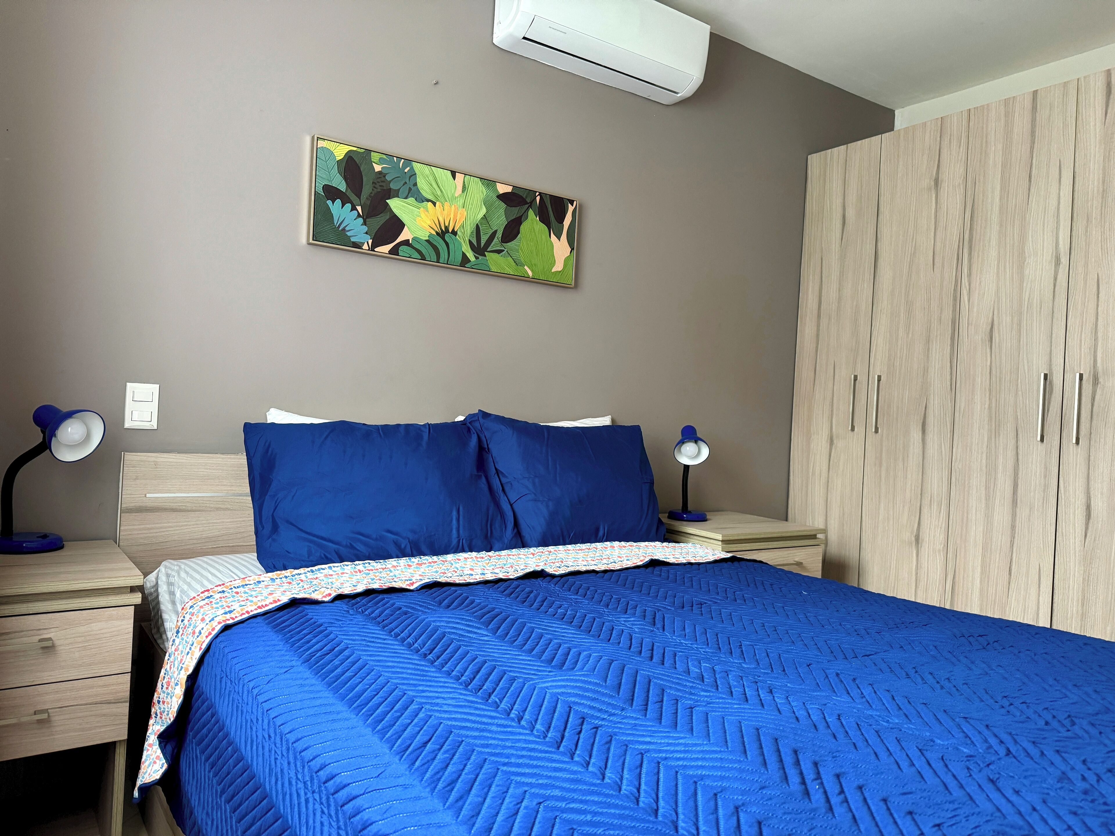 Ein Schlafzimmer mit einem Bett, zwei Nachttischen mit Lampen, einem Kleiderschrank und einer Wandklimaanlage.
