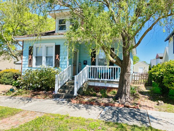 A two-story house with a front porch, a small attached garage, and a tree in front.