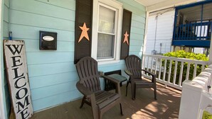 Une véranda avec deux fauteuils Adirondack, une petite table et une pancarte indiquant « BIENVENUE ».