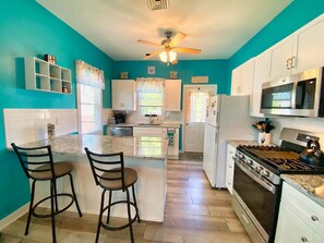 A kitchen with a central island, white cabinets, a stove, and a ceiling fan.