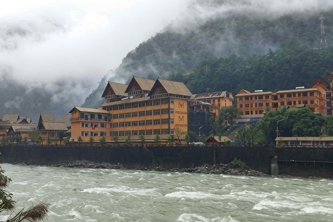 A hotel with multiple stories, a waterfront view, and a mountainous backdrop.