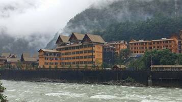 A hotel with multiple stories, a waterfront view, and a mountainous backdrop.