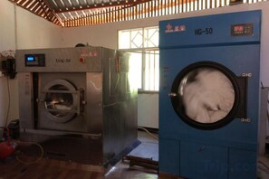 Two industrial washing machines, one labeled 'XQ-50' and the other 'HG-50,' in a room with a wooden floor and a window with bars.