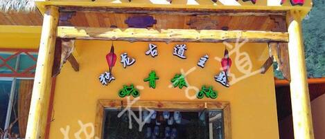 A hotel entrance with a yellow facade, a signboard with Chinese characters, and a thatched roof.