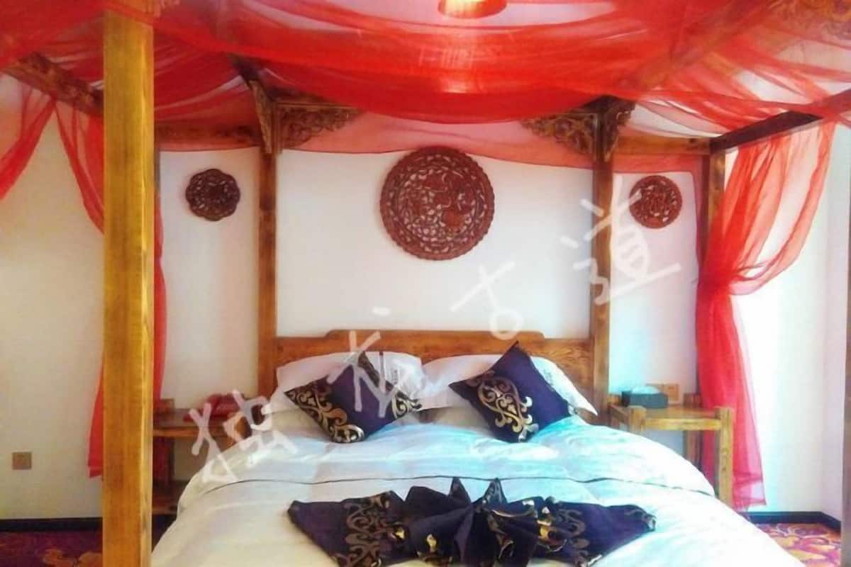 A room with a bed, red drapes, wooden beams, and decorative wall plates.