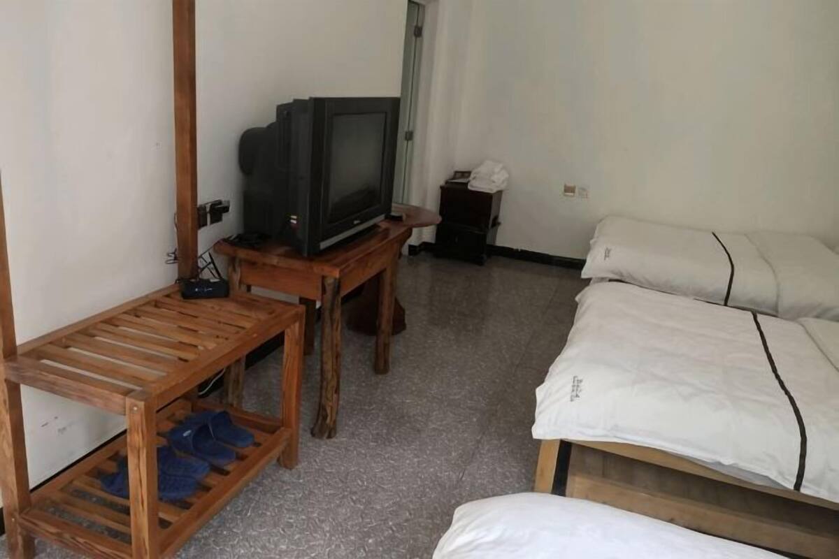 A room with a bed, a TV on a wooden stand, a small table, and a door.