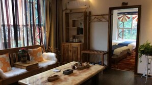 Una habitación con sofá, mesa de madera, espejo, cama y ventana con cortinas.