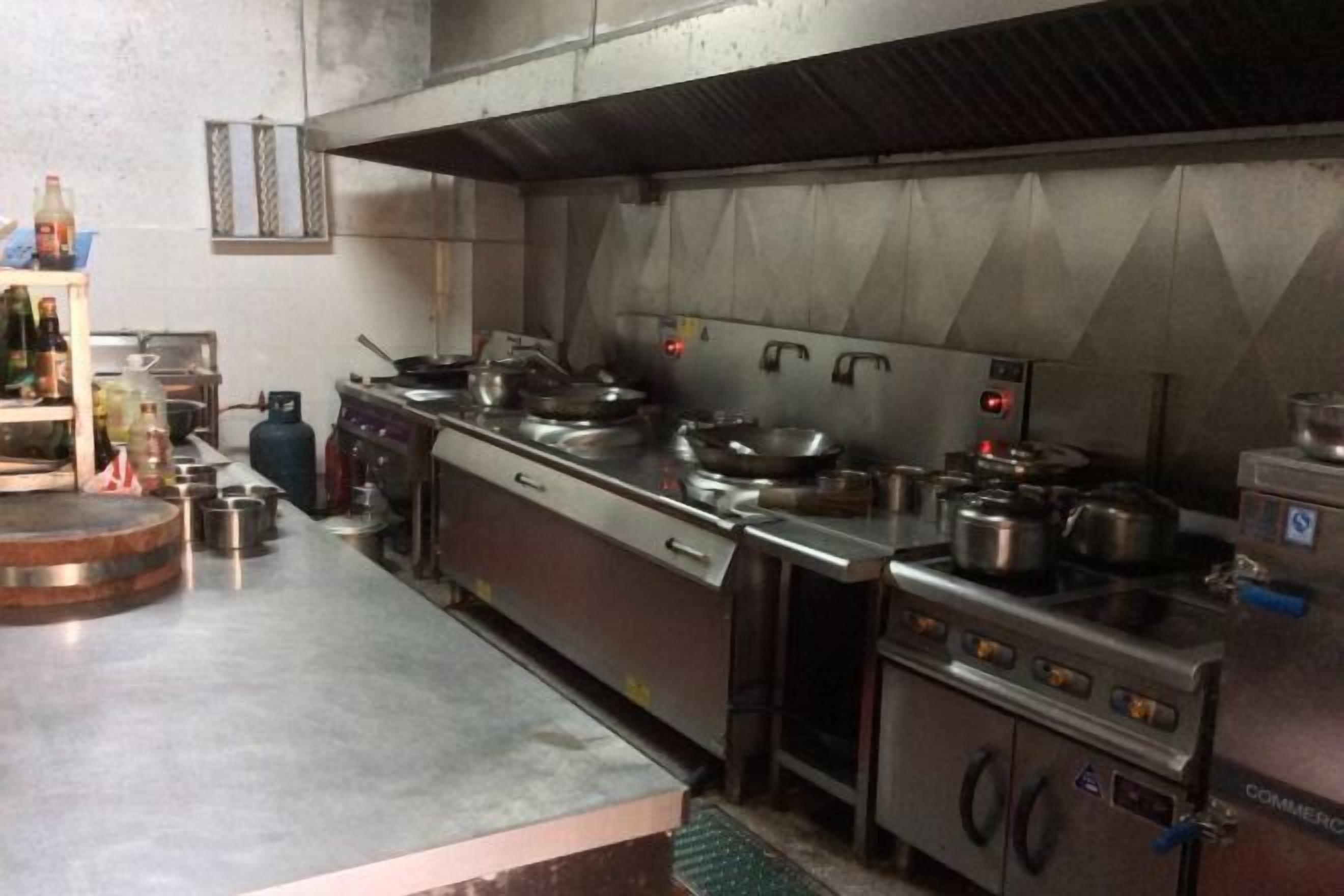 A commercial kitchen with stainless steel appliances, including a stove, pots, and a refrigerator.