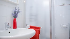 Ein Badezimmer mit einem weißen Waschbecken, einer roten Vase mit Lavendel und einem roten Handtuch.