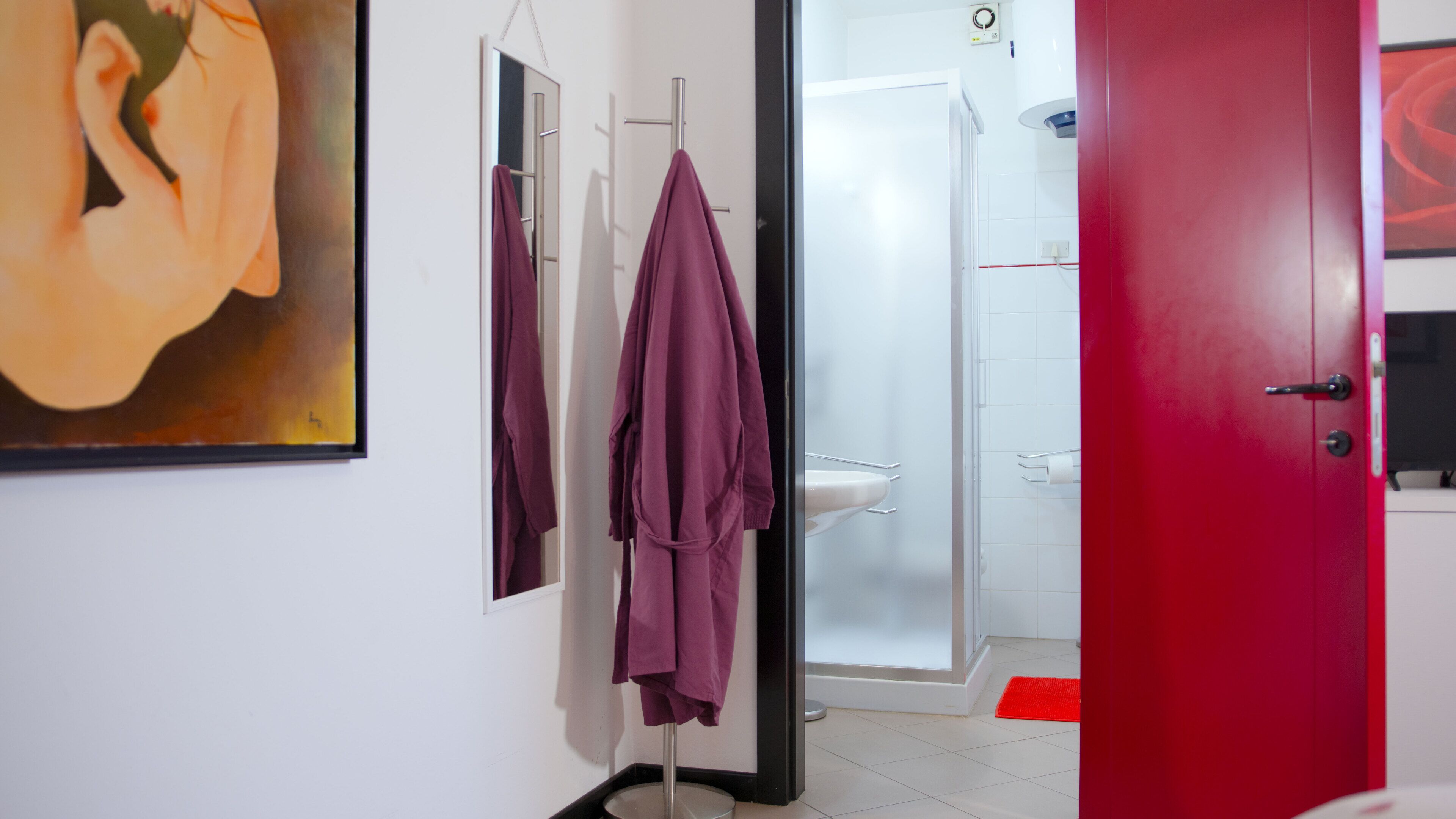 Un bagno moderno con cabina doccia in vetro, un lavandino bianco e una porta rossa.