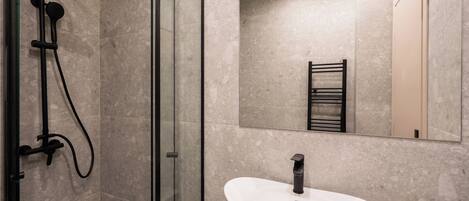 A modern bathroom with a glass-enclosed shower, a white sink, and a large mirror.