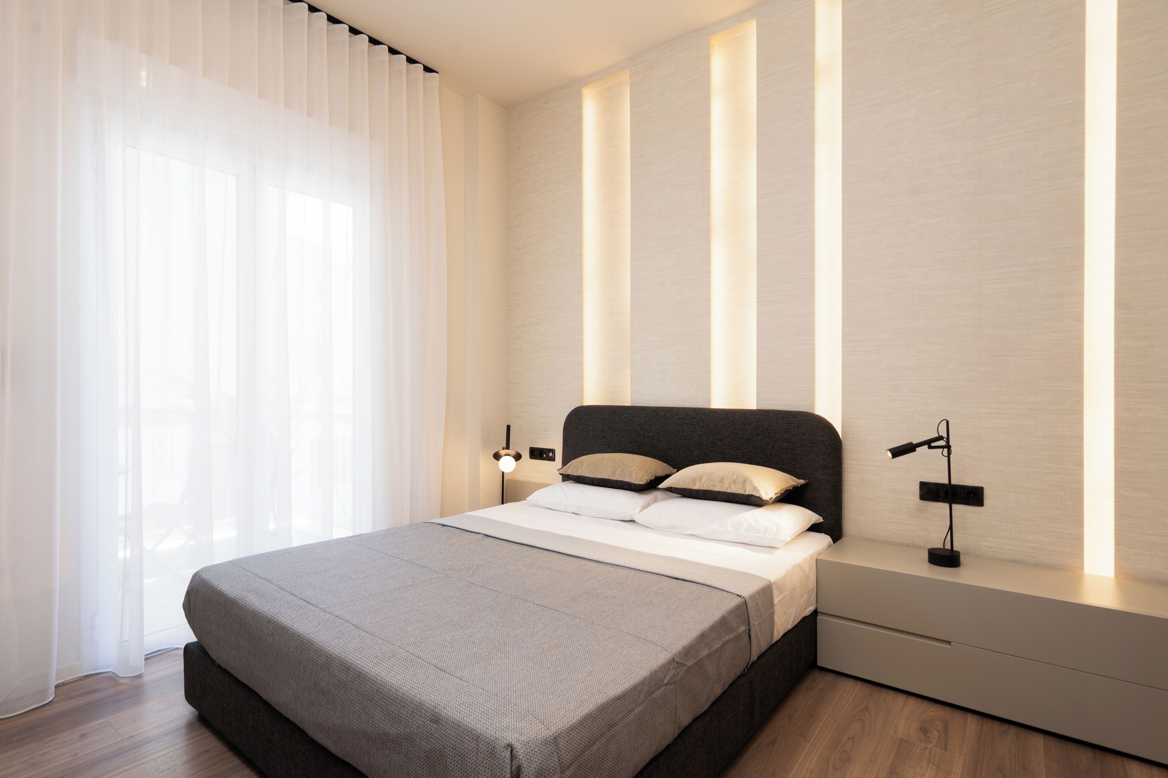 A modern bedroom with a large bed, bedside tables, and a nightstand with a lamp.