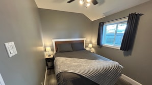 A bedroom with a bed, nightstands, a window with curtains, and a ceiling fan. - Relaxing Graham Lake Escape (Mallorytown)