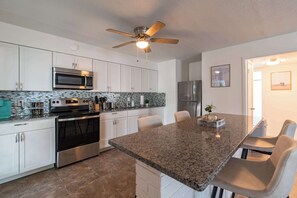 A modern kitchen with white cabinets, stainless steel appliances, a granite countertop, and a ceiling fan.