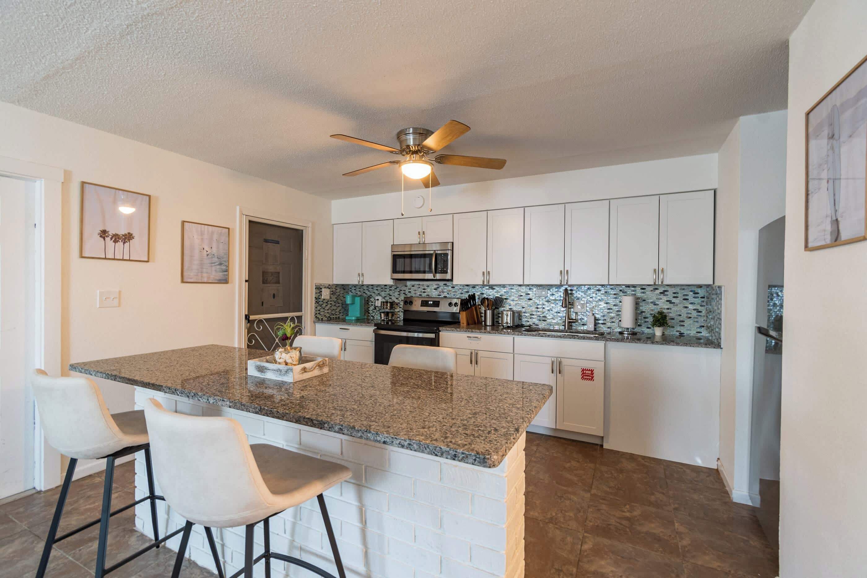 Een moderne keuken met een centraal eiland, witte kasten en een plafondventilator.
