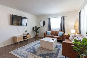 A living room with a flat-screen TV, two sofas, a coffee table, a potted plant, and a mirror.