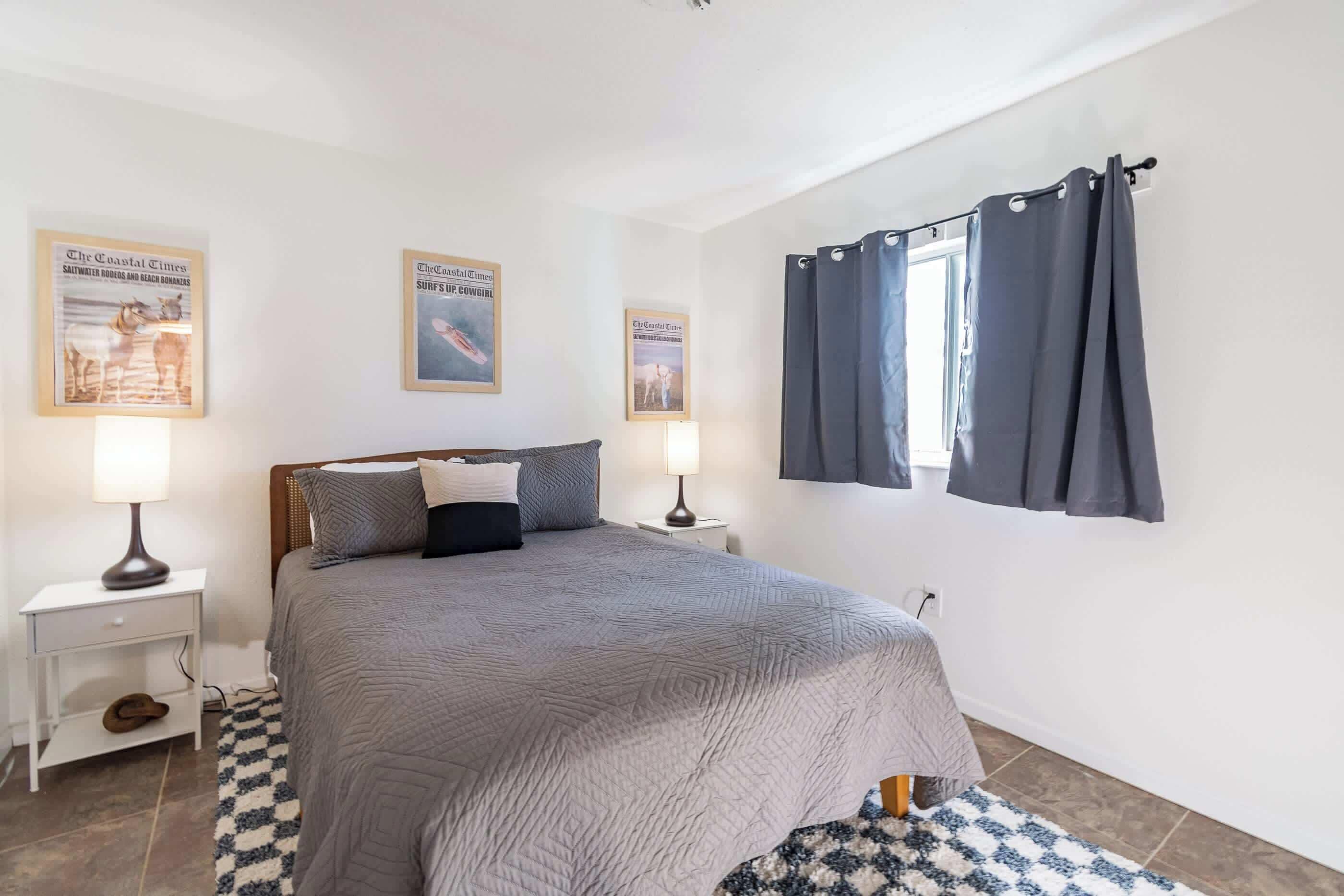 A bedroom with a bed, two nightstands, a window with curtains, and three framed pictures on the wall.