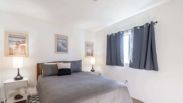 A bedroom with a bed, two nightstands, a window with curtains, and three framed pictures on the wall.