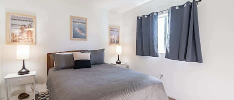 Una camera da letto con un letto, due comodini, una finestra con tende e tre quadri appesi al muro.
