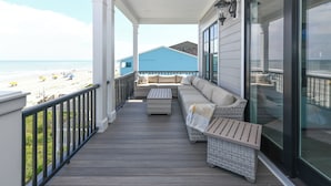 Un balcon fermé avec vue sur la plage, des meubles en osier et une porte vitrée.