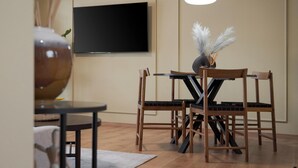 A modern living room with a flat-screen TV mounted on the wall, a round wooden table with chairs, and a decorative vase with feathers. - Aria Luxury Apartment  (Patras)