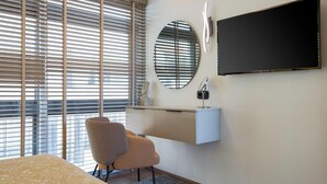 A modern hotel room with a bed, a desk with a chair, a television, and large windows with blinds. - Aria Luxury Apartment  (Patras)