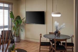 Un coin repas avec une table ronde, des chaises, une plante en pot et un téléviseur à écran plat fixé au mur.