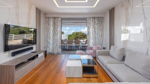 A modern living room with a flat-screen TV, a sofa, a coffee table, and a dining area visible through a glass door. - Villa Lantana (Zadar)