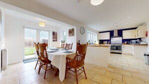 A spacious kitchen with modern appliances, a dining area with wooden chairs, and a view of the backyard through large windows. - 5-bedroom Home - Sleeps 16 - Ideal for Groups (Doncaster)