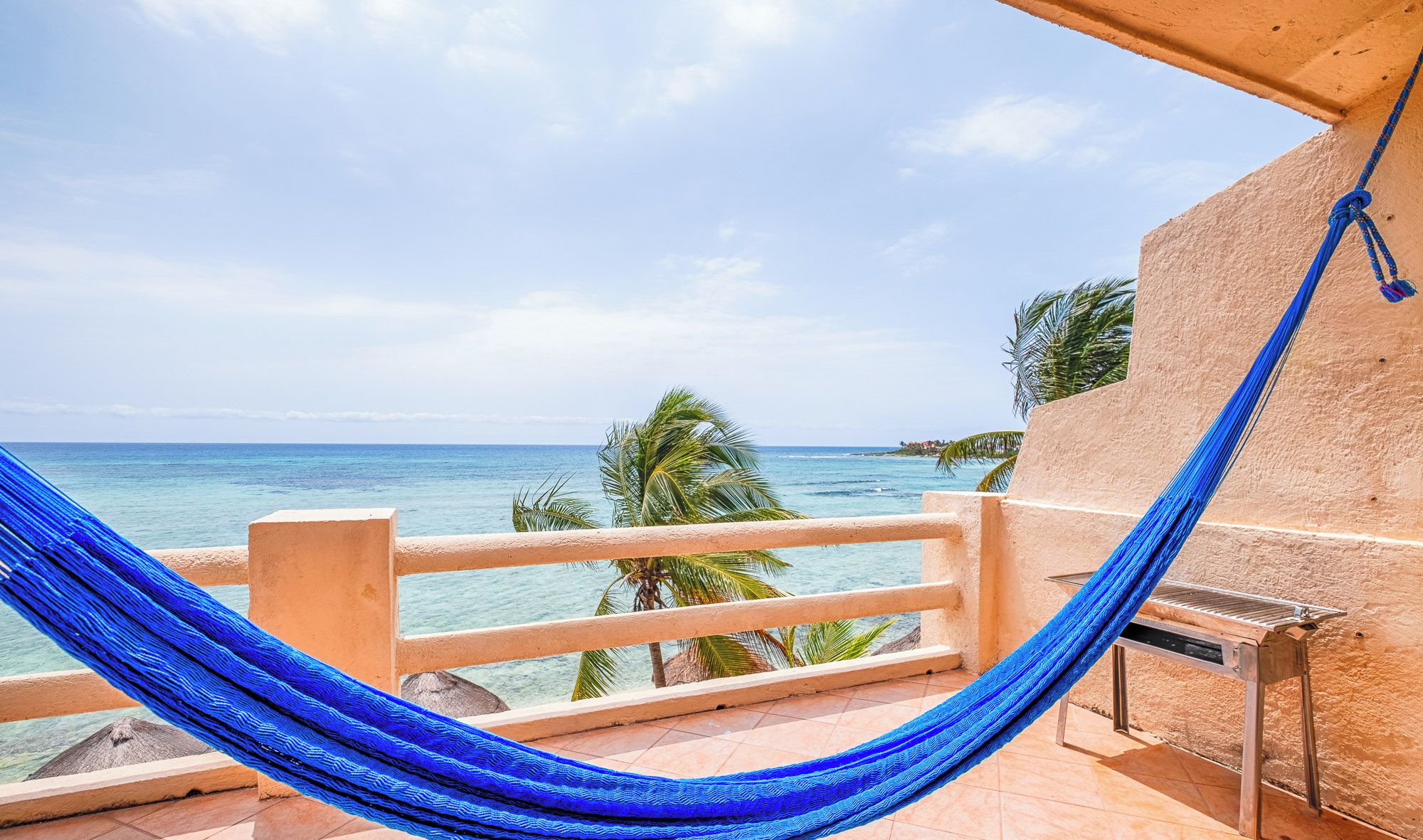 Een hangmat op een balkon met uitzicht op een strand, palmbomen en de oceaan.