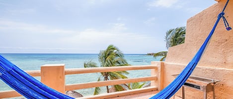 A hammock on a balcony overlooking a beach with palm trees and the ocean.