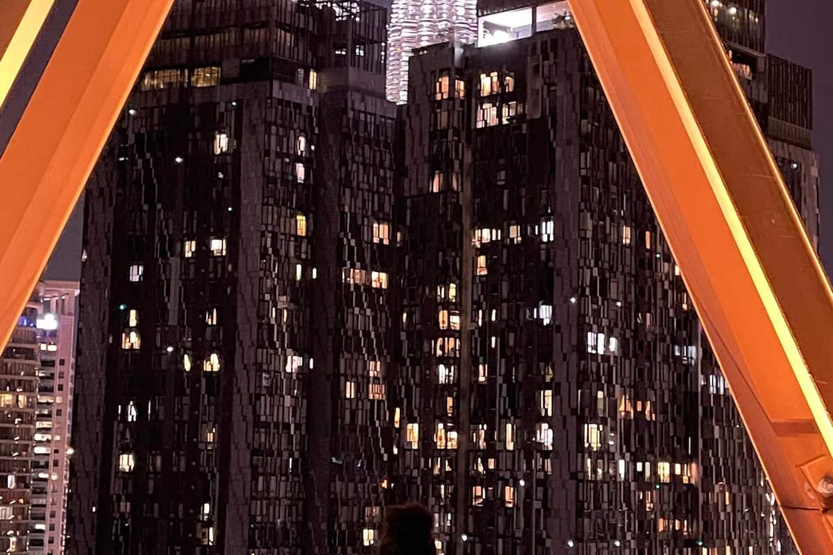 Vista nocturna d'un edifici amb dues agulles il·luminades, una piscina d'aigua cristal·lina i una persona a la piscina.
