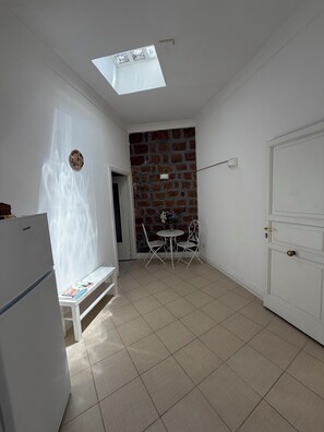 A kitchen with a refrigerator, a bench, a dining table with chairs, a brick wall, and a door. - Apartment in the Historic Center of Naples: Viviani Terrace (Napoli)