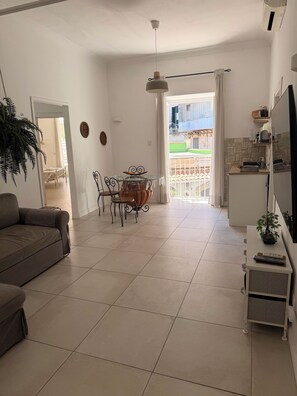 A living room with a sofa, a dining table with chairs, a TV on a stand, and a kitchen area with a fridge. - Apartment in the Historic Center of Naples: Viviani Terrace (Napoli)