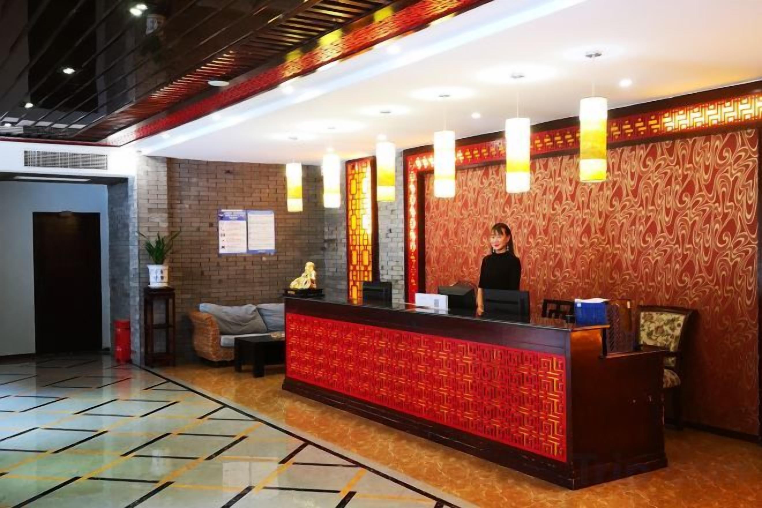 A hotel reception area with a reception desk, a receptionist, and a patterned wall.