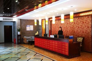 Zona de recepción de un hotel con mostrador, recepcionista y un papel tapiz estampado.