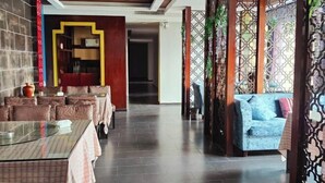 Un restaurante con mesas cubiertas de manteles a cuadros, un sofá azul y un separador decorativo con diseños intrincados.