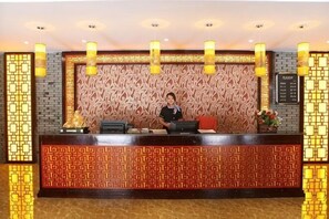Een receptiebalie met een patroonachtergrond, een receptionist en een prikbord met tekst.