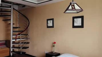 Quarto com cama, mesa de cabeceira, um vaso com uma única rosa, um quadro emoldurado, outro quadro emoldurado e uma escadaria em espiral.