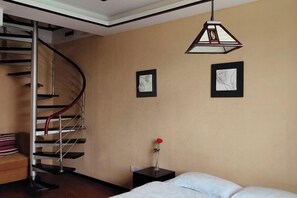 A bedroom with a bed, a nightstand, a vase with a single rose, a framed picture, a second framed picture, and a spiral staircase. - Yunxi Yard Hotel (Youyang County)