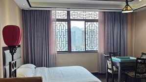 Una habitación de hotel con una cama, un escritorio con una silla, una silla roja y una ventana con cortinas.