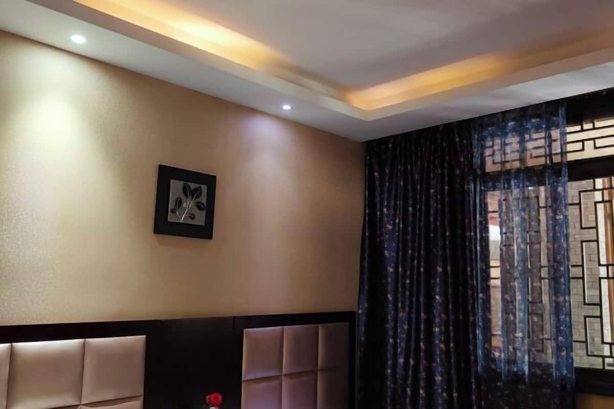 A hotel room with a padded headboard, a framed picture on the wall, and a window with patterned curtains.