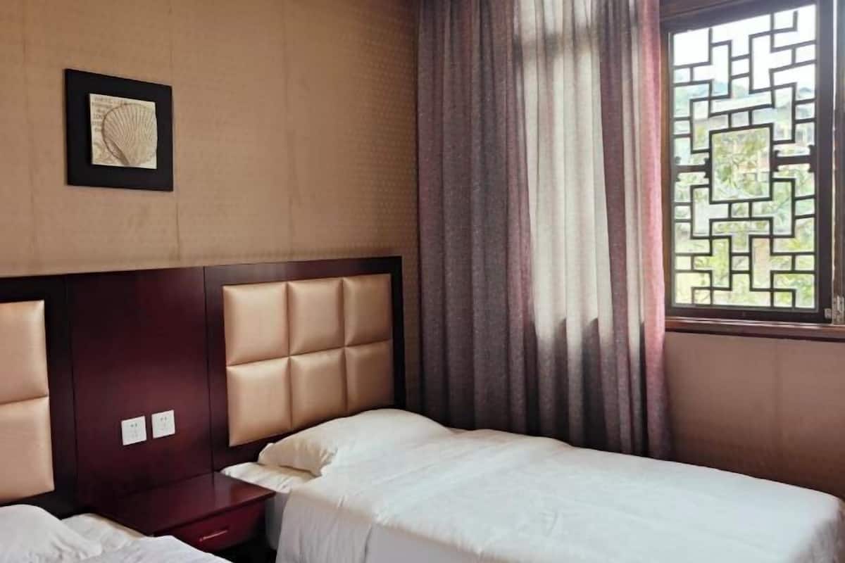 A hotel room with a bed, a nightstand, and a window with a geometric pattern.