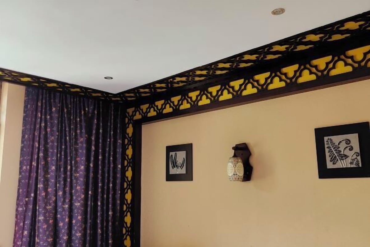 A room with a patterned curtain, a wall with a decorative black and yellow border, and two framed pictures.