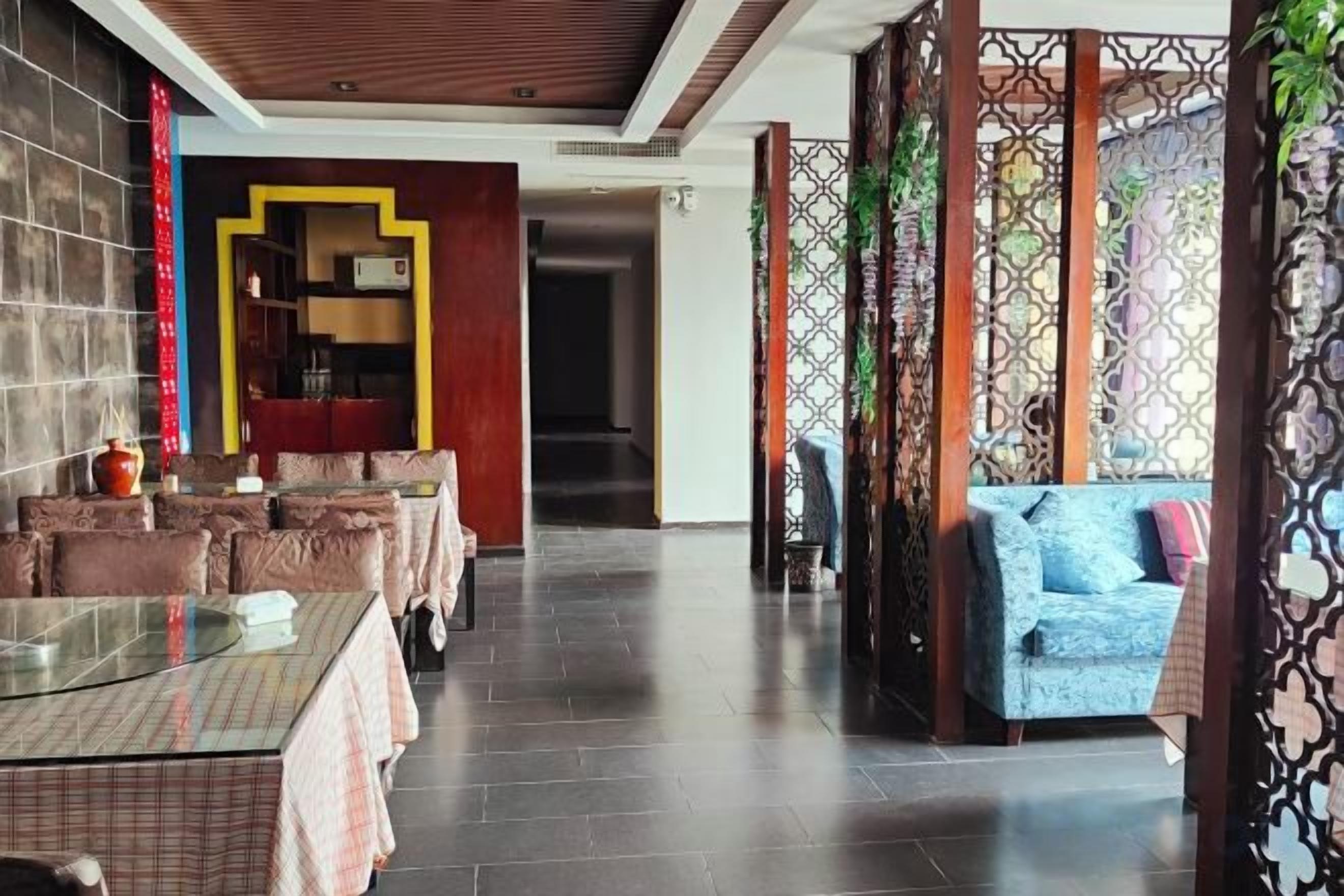 Un restaurante con una larga mesa, asientos acolchados, un sofá y un separador decorativo.
