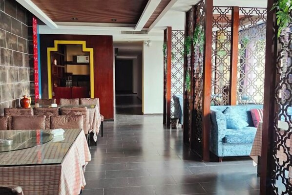 A restaurant with a long table and cushioned seating, a sofa, and a decorative partition. - Yunxi Yard Hotel (Youyang County)