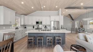 A modern kitchen with white cabinetry, a central island with bar stools, and a dining area with a wooden chair and a patterned sofa.