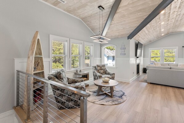 A spacious living room with a high ceiling, a staircase with a metal railing, and a large window providing natural light.